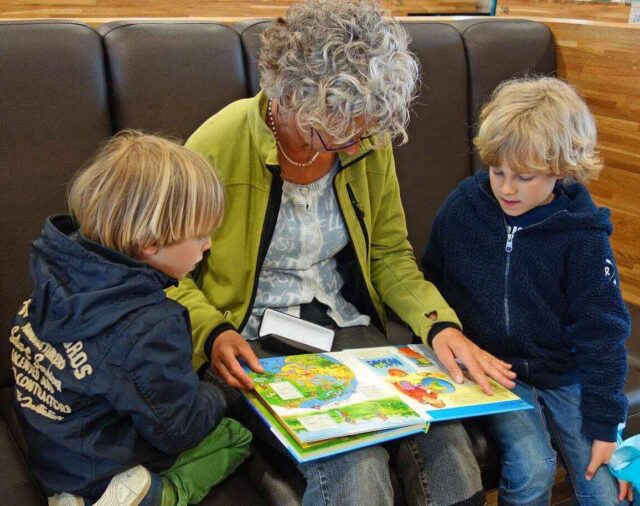 A grandparent reads to two of their grandchildren